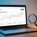 Ordinateur portable présentant une refonte visuelle de boutique en ligne avec des indicateurs abstraits de baisse et de récupération du référencement, accompagné d’une loupe et d’outils de travail.